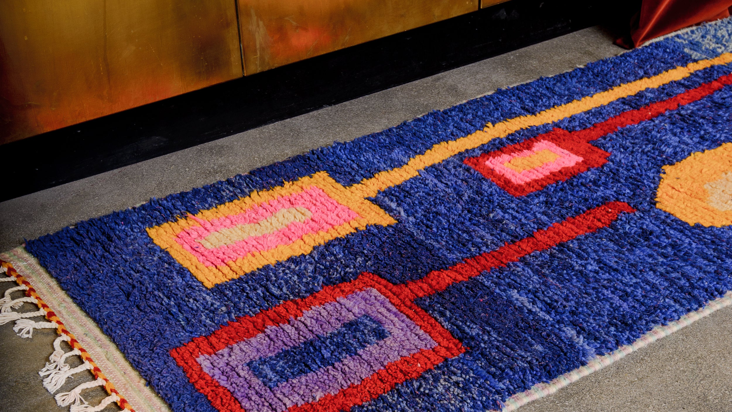 Wool runner rug laying on concrete floor in front of a black kitchen.
