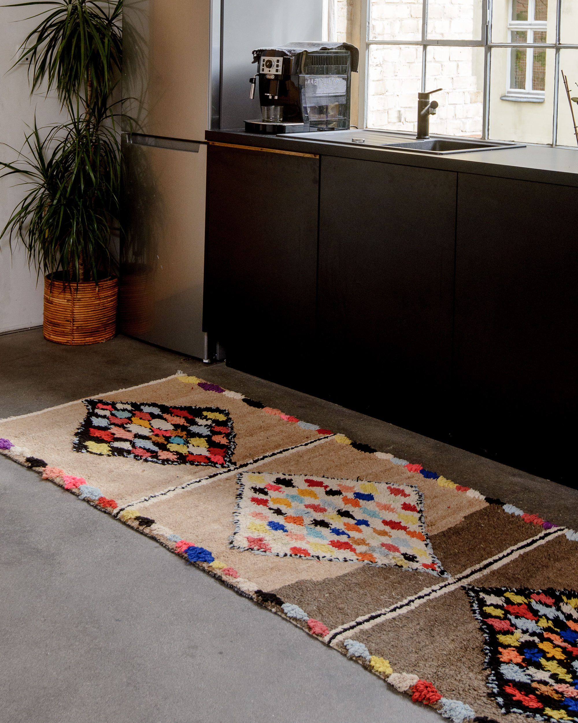 Wool runner rug laying on concrete floor in front of a black kitchen.