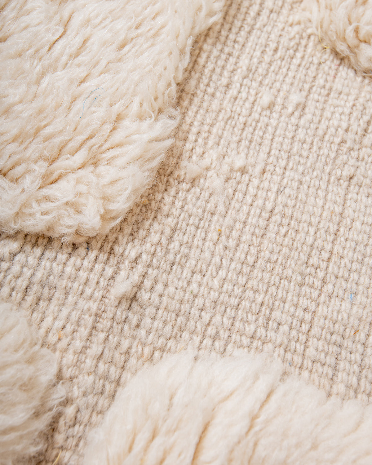 Close up of wool cream rug with contrasting woven and knotted areas. 