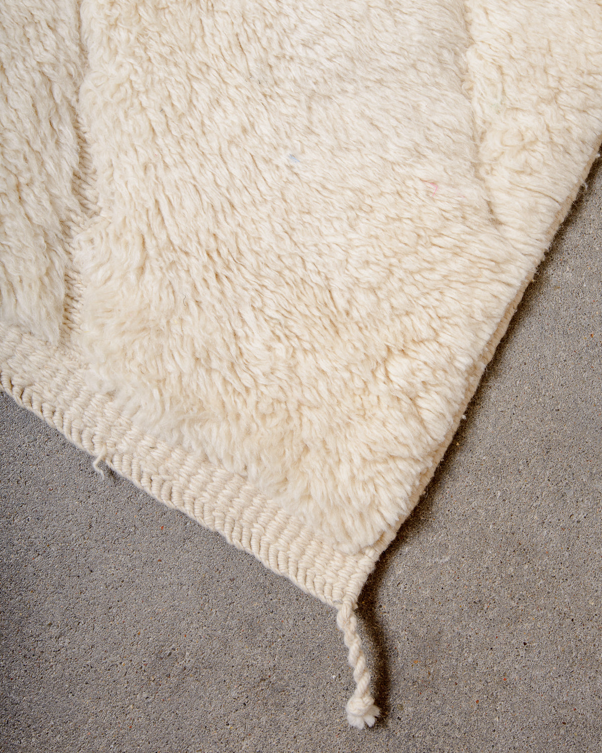Corner of cream M'rirt rug with tightly woven edges and one corner tassel.