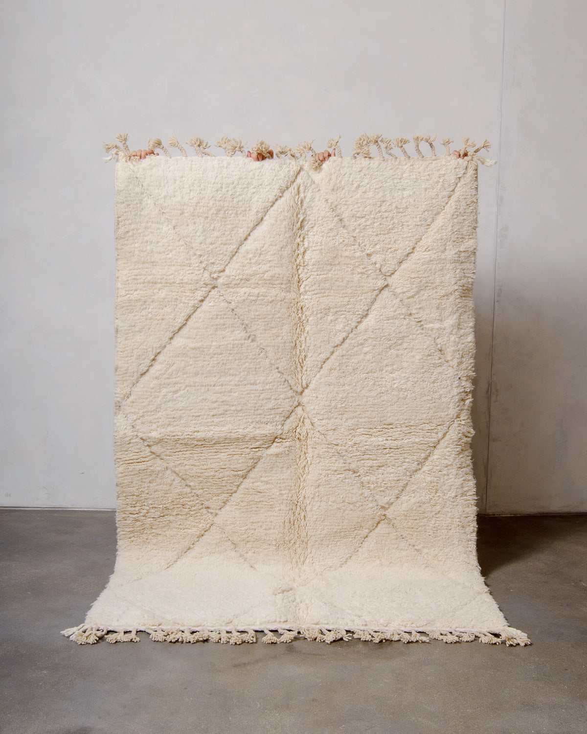 Cream wool rug with woven diamond pattern being held up in front of a white wall.