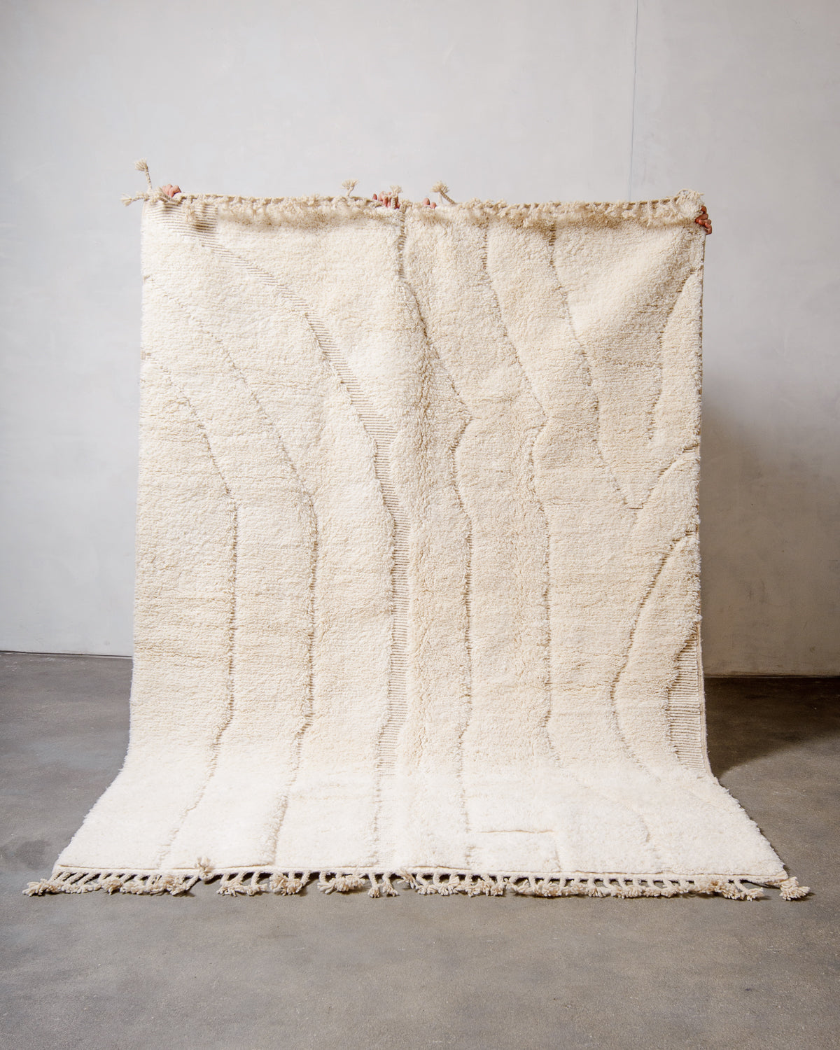 Cream wool rug with woven pattern being held up in front of a white wall.