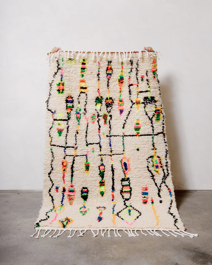 Berberlin Azilal rug made of sheep’s wool and neon cotton being held up against a white studio wall.