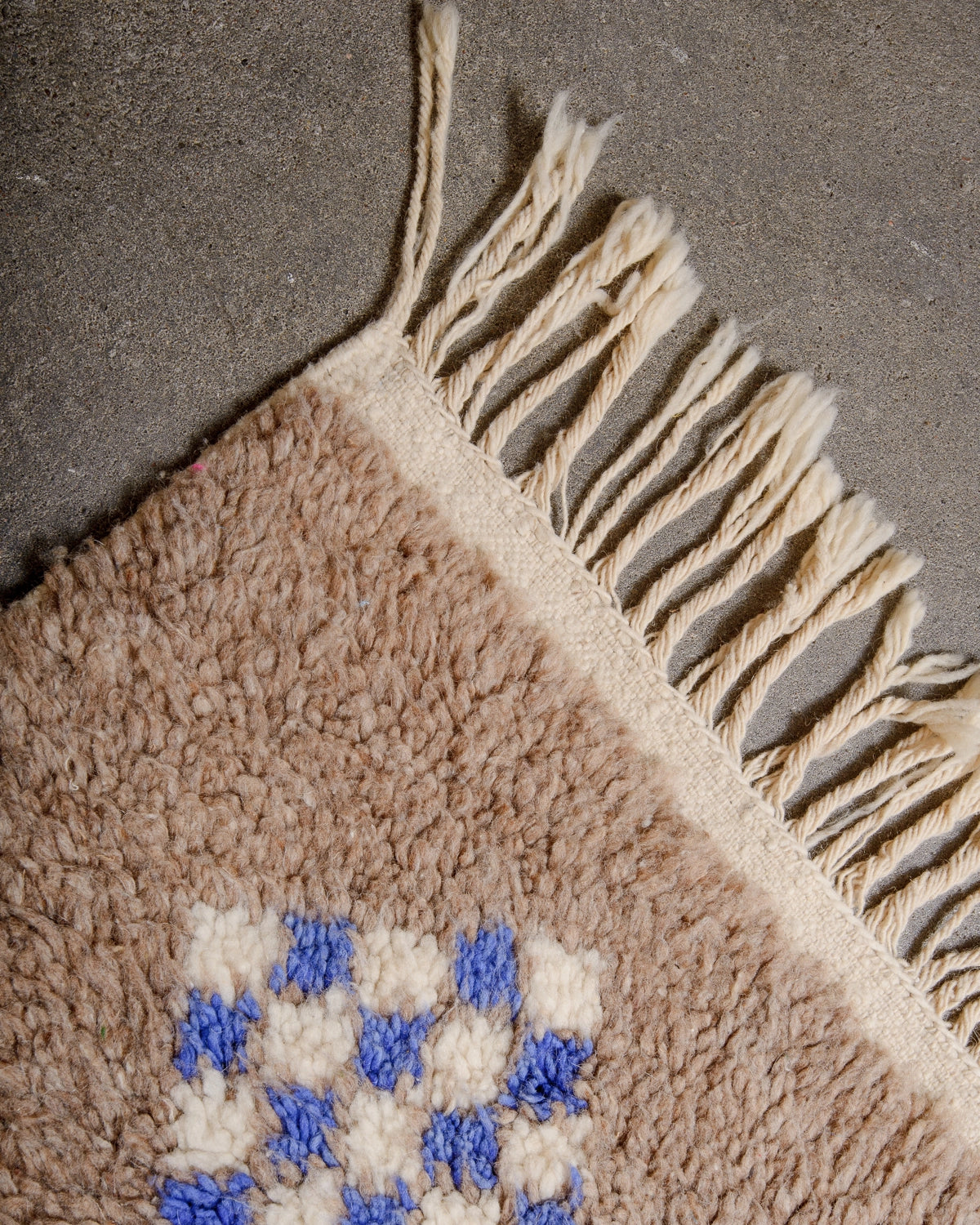 Natural wool tassels on a Berberlin Vintage Berber Rug made of fluffy brown wool with faded blue, red, yellow and white design details.