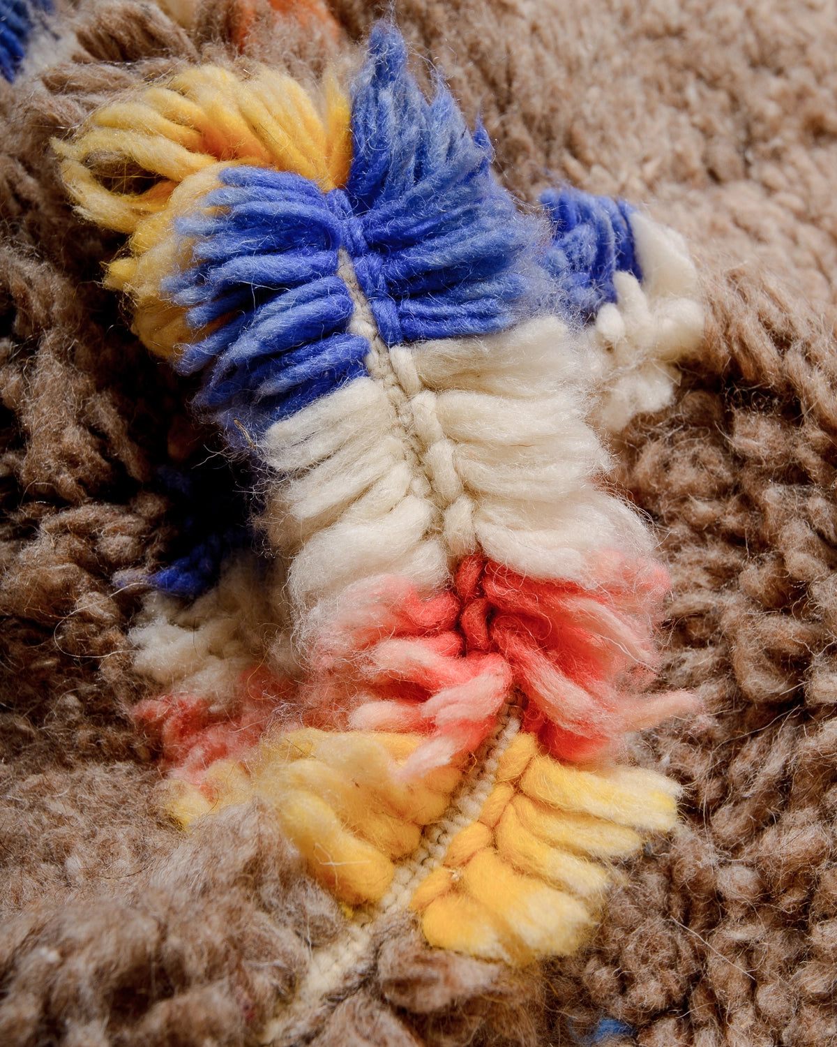 Details on a Berberlin Vintage Berber Rug made of fluffy brown wool with faded blue, red, yellow and white design.