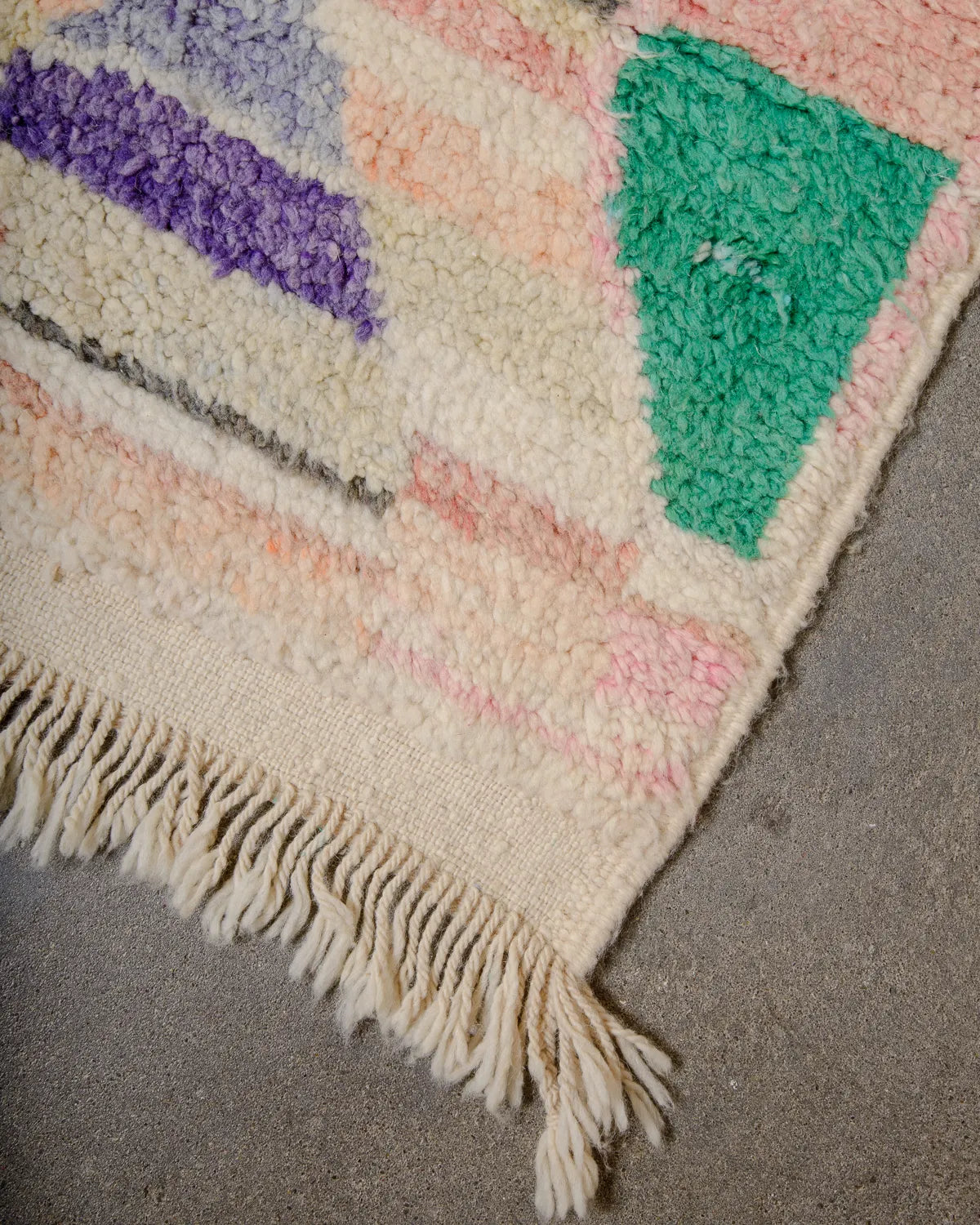 Tasseled edge of vintage wool Boujad rug laying on concrete studio floor.