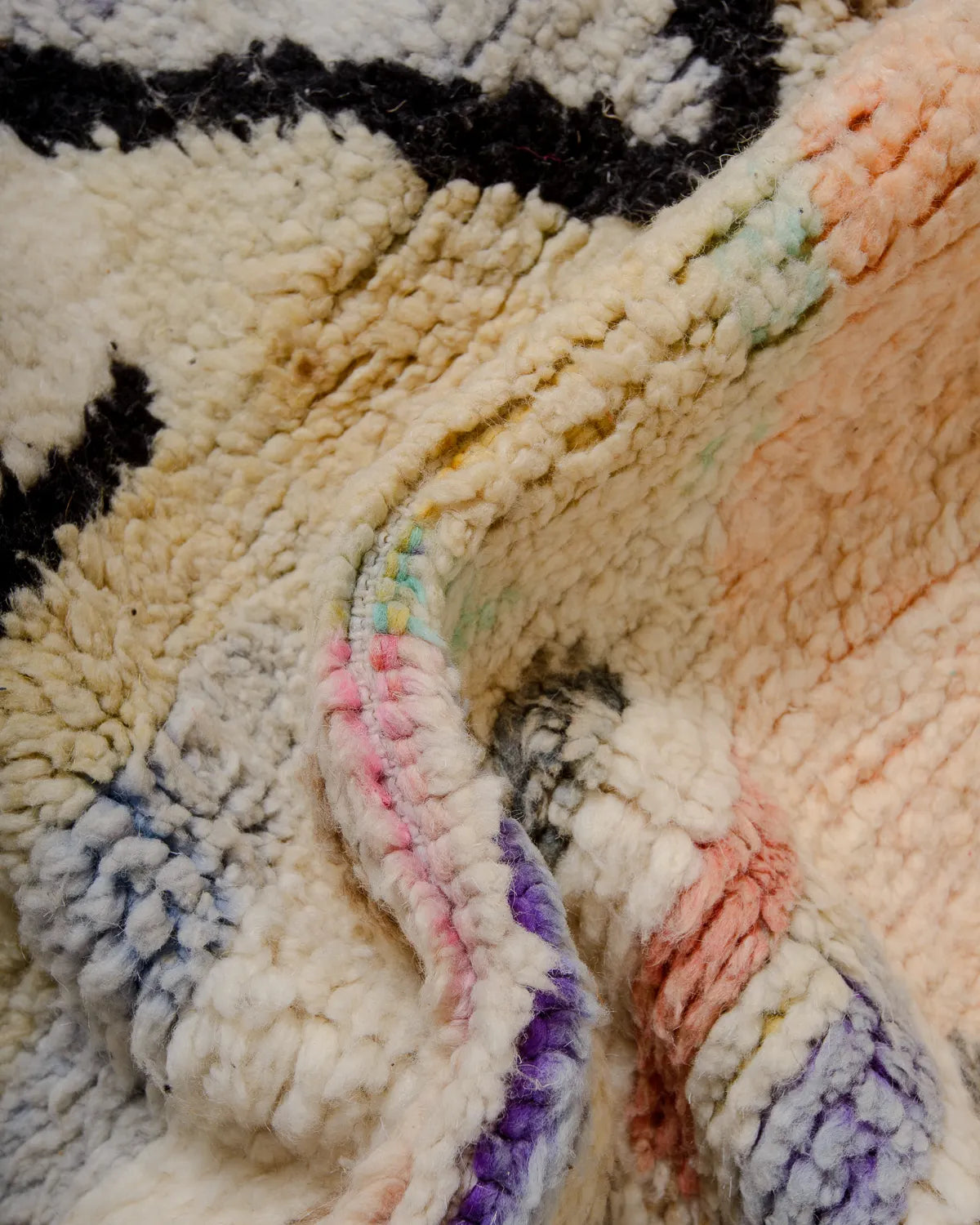 Detail of wool Berber rug featuring faded shades of pink, blue, purple, yellow and orange.