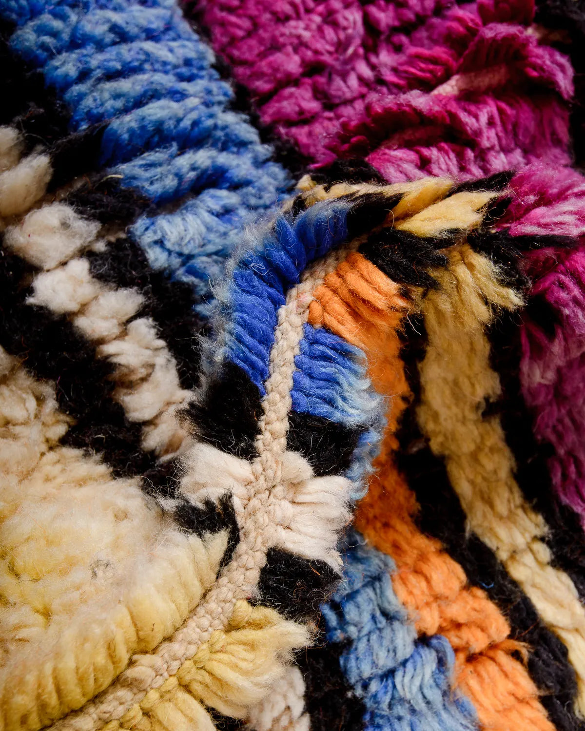 Detail of wool Berber rug featuring a modern design in shades of pink, yellow, orange, blue and black.
