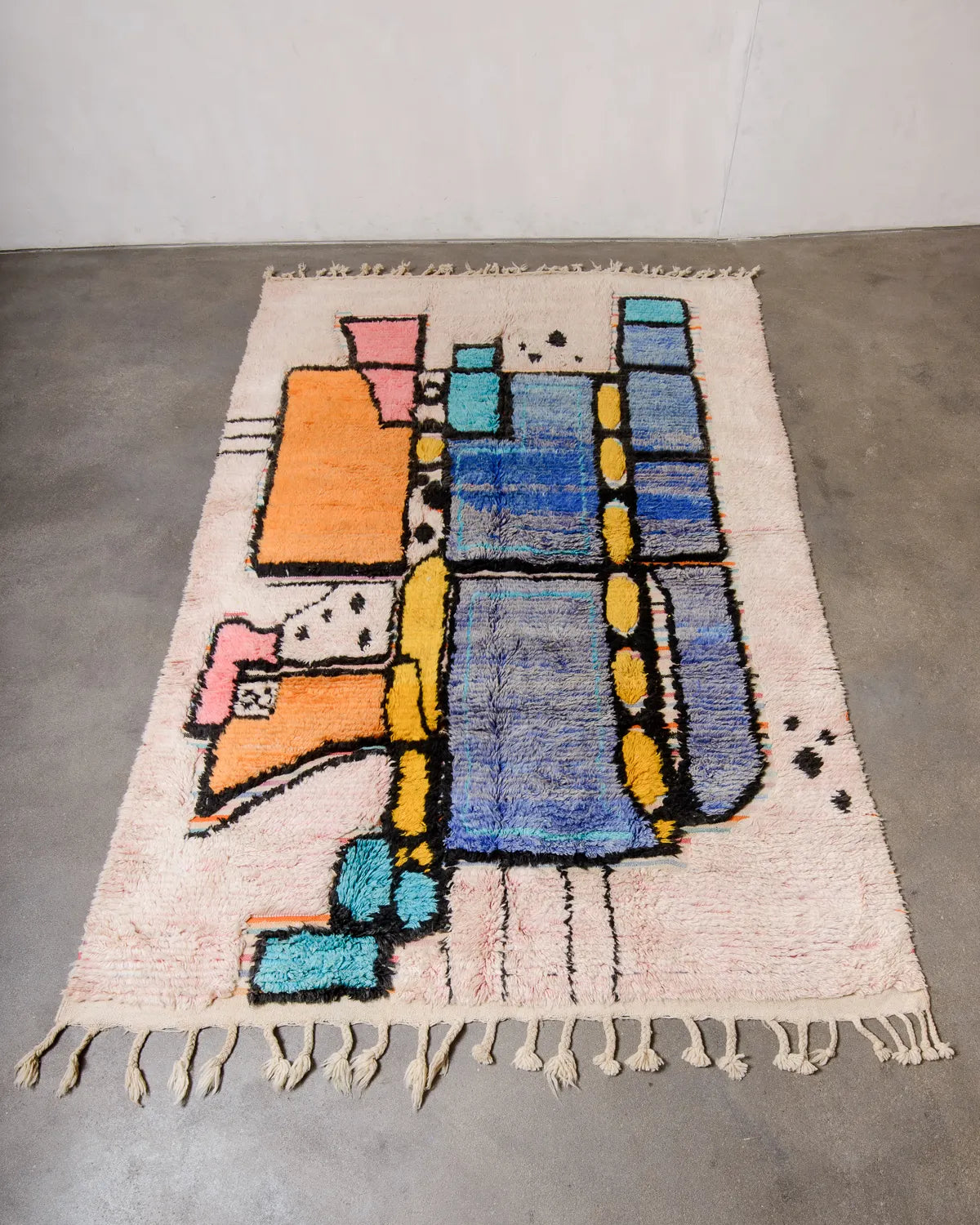 Berberlin Boujad rug handwoven from fluffy wool in shades of blue, turquoise, orange, pink and black, with flat-woven sections in stripes, laying flat on cement floor. 