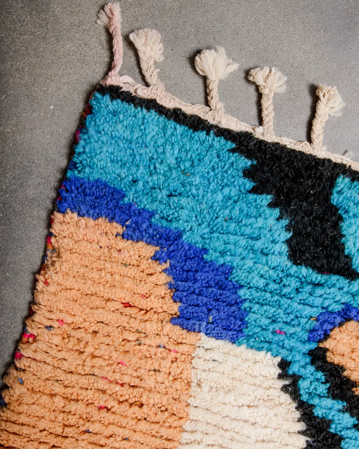 Natural cream wool tassels on the end of a rug that is made of blue, black and apricot coloured wool.