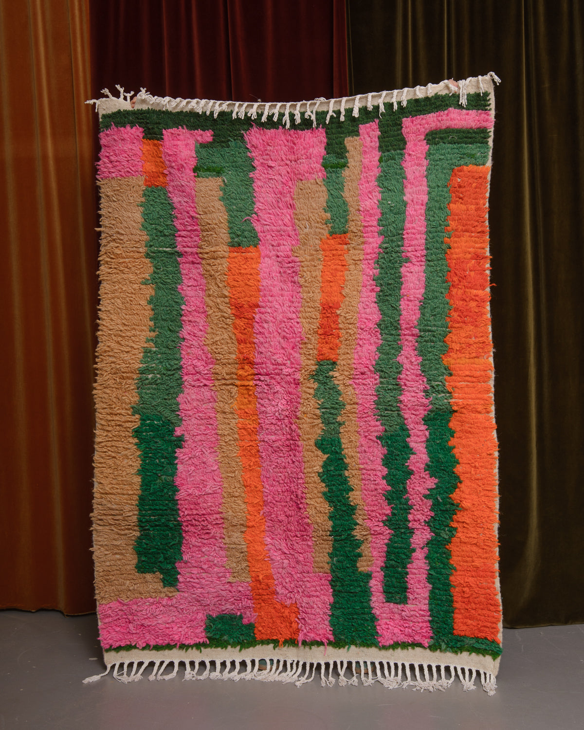Azilal rug held in front of velvet curtains. 