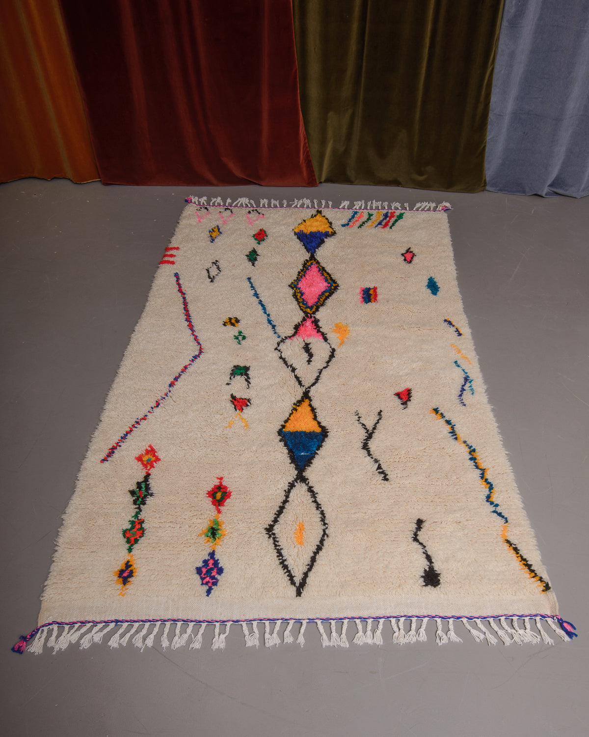 Azilal rug featuring colourful design on a grey floor in front of curtains.