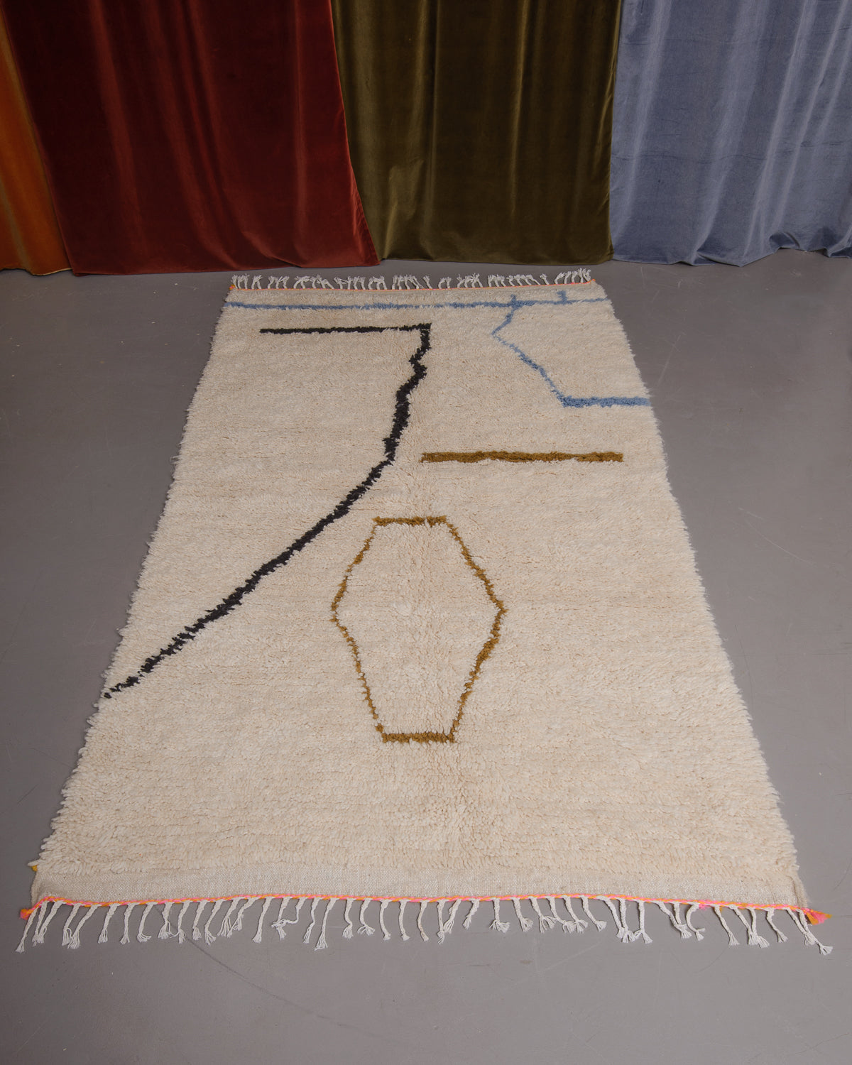 Azilal rug featuring colourful design on a grey floor in front of curtains.