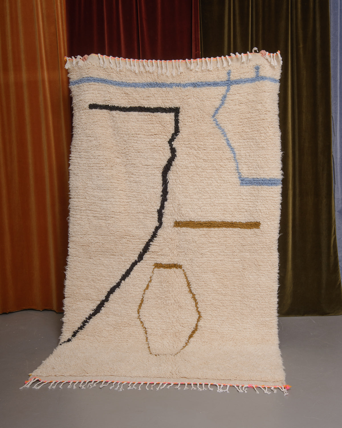 Azilal rug held in front of velvet curtains. 