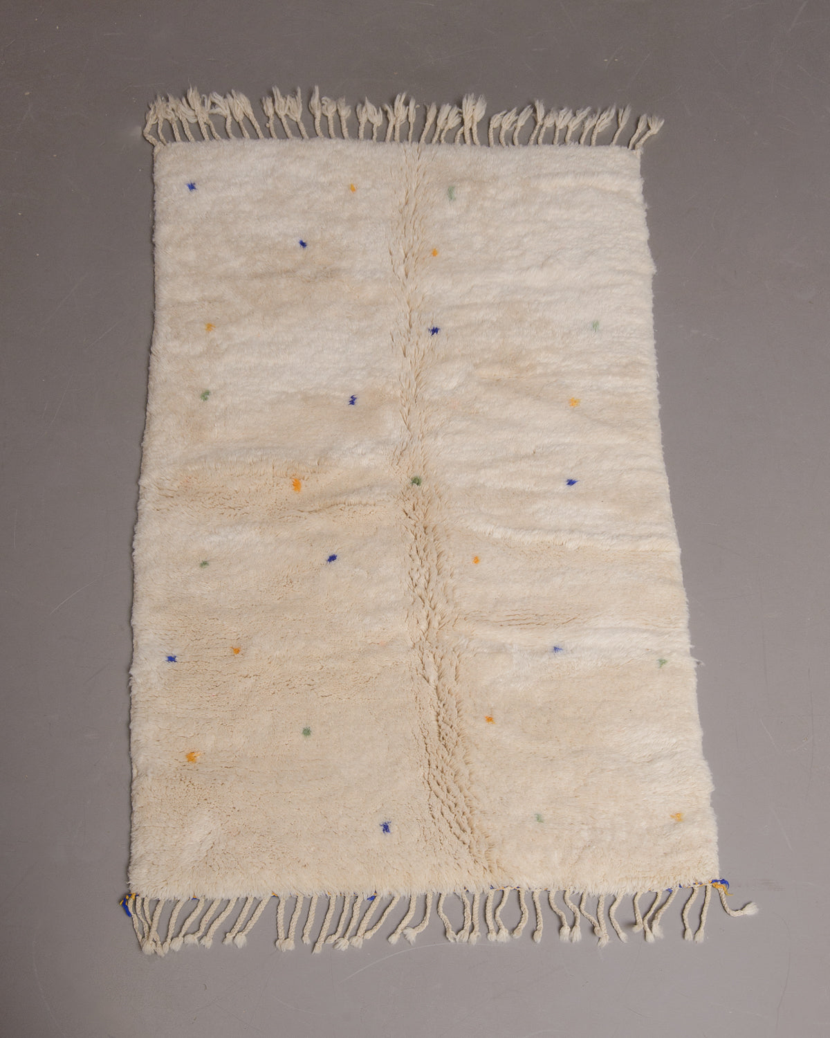 Berberlin Finest rug with cream wool and softly coloured dots, on a grey floor. 
