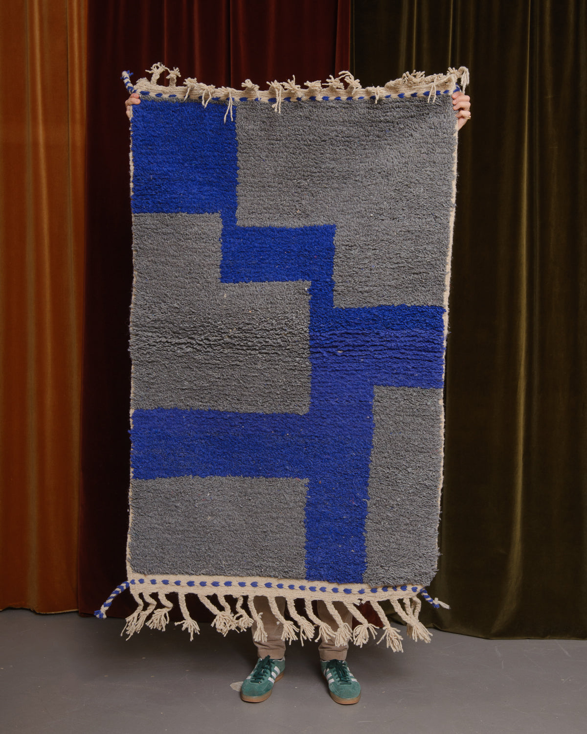 Berberlin Special Edition Beniourain rug held up in front of a velvet curtain.