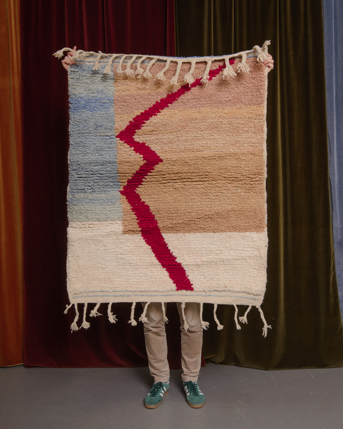 Berberlin Special Edition Beniourain rug held up in front of a velvet curtain.
