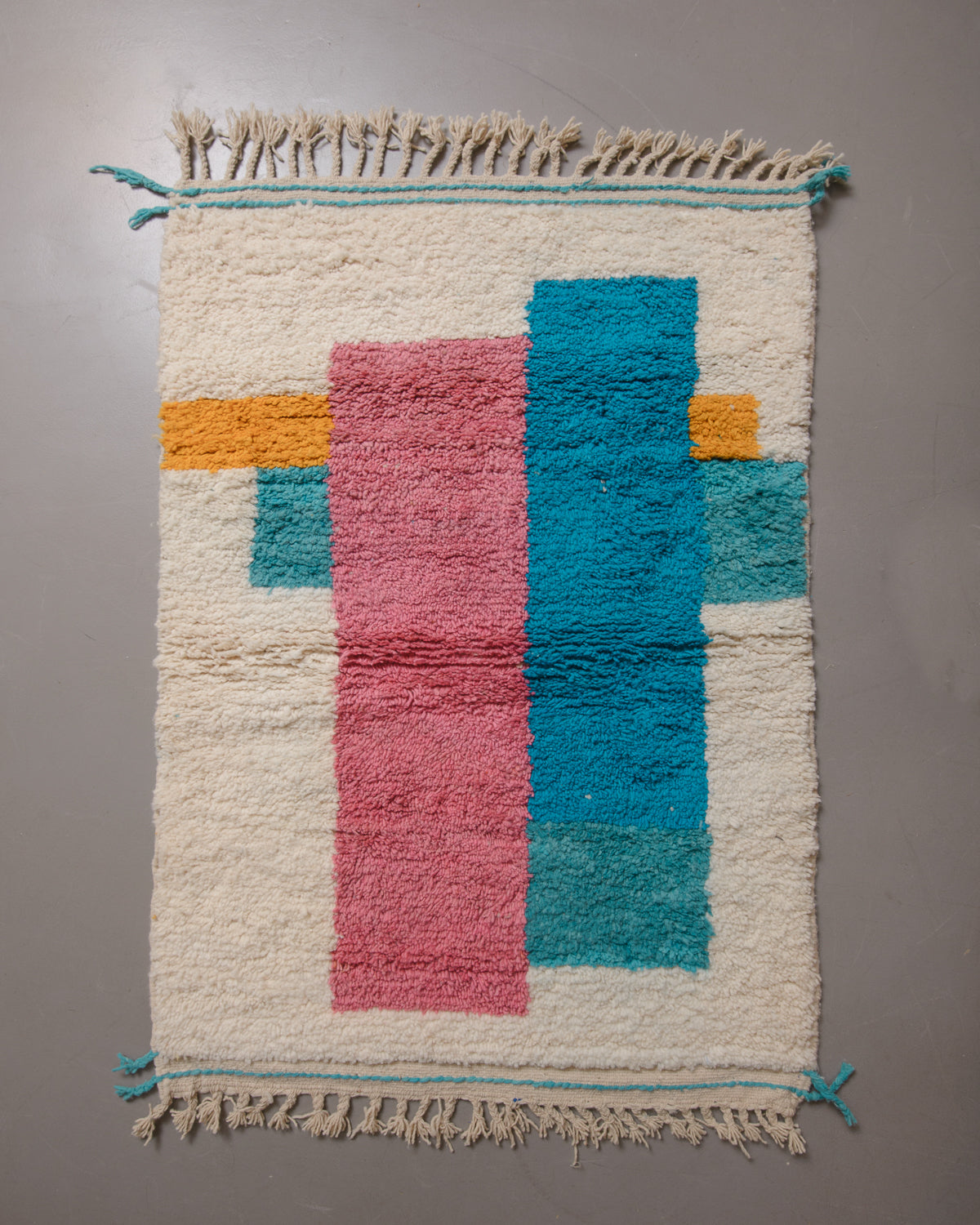 Wool rug with cream tassels on a grey floor.