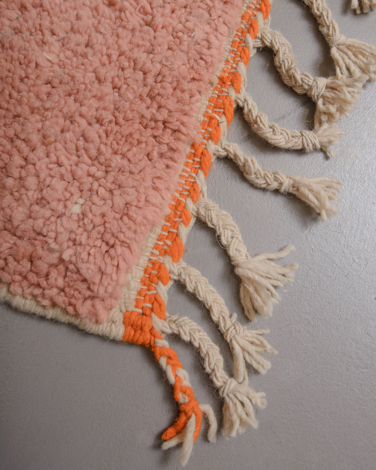 Corner of Berberlin rug with natural wool tassels and orange braiding along the edge..