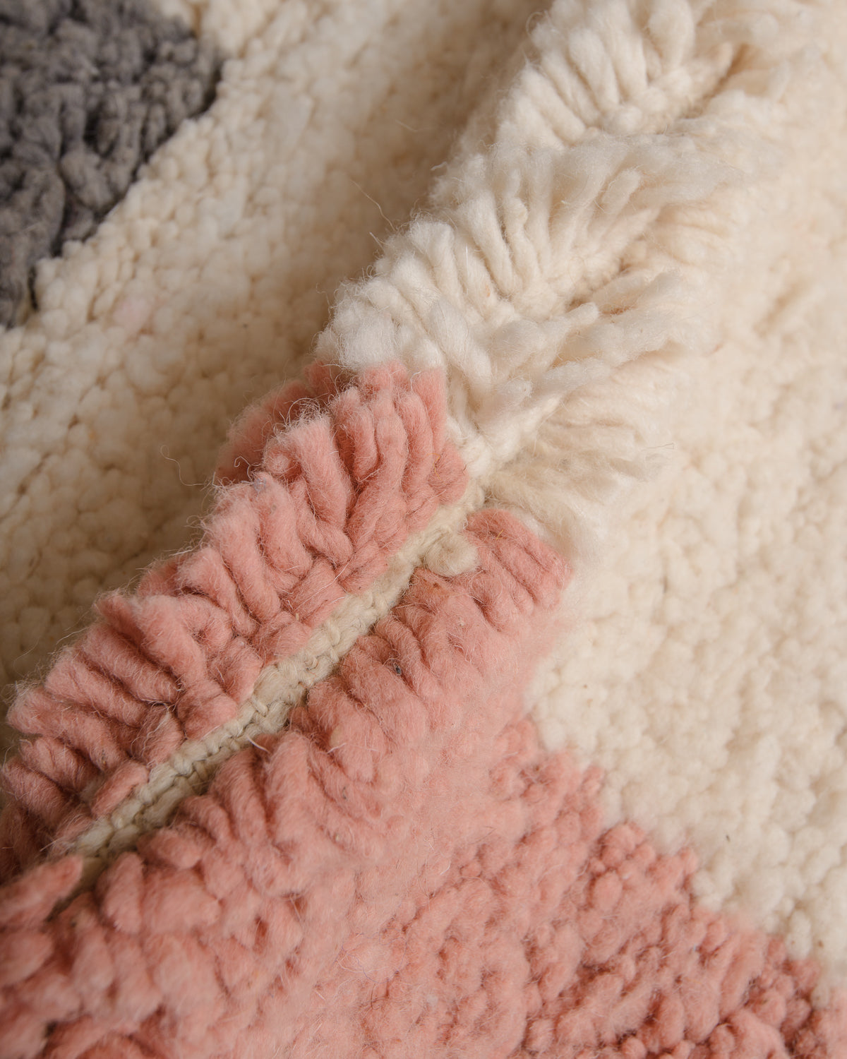 Close up of cream wool rug with pink and grey details. 