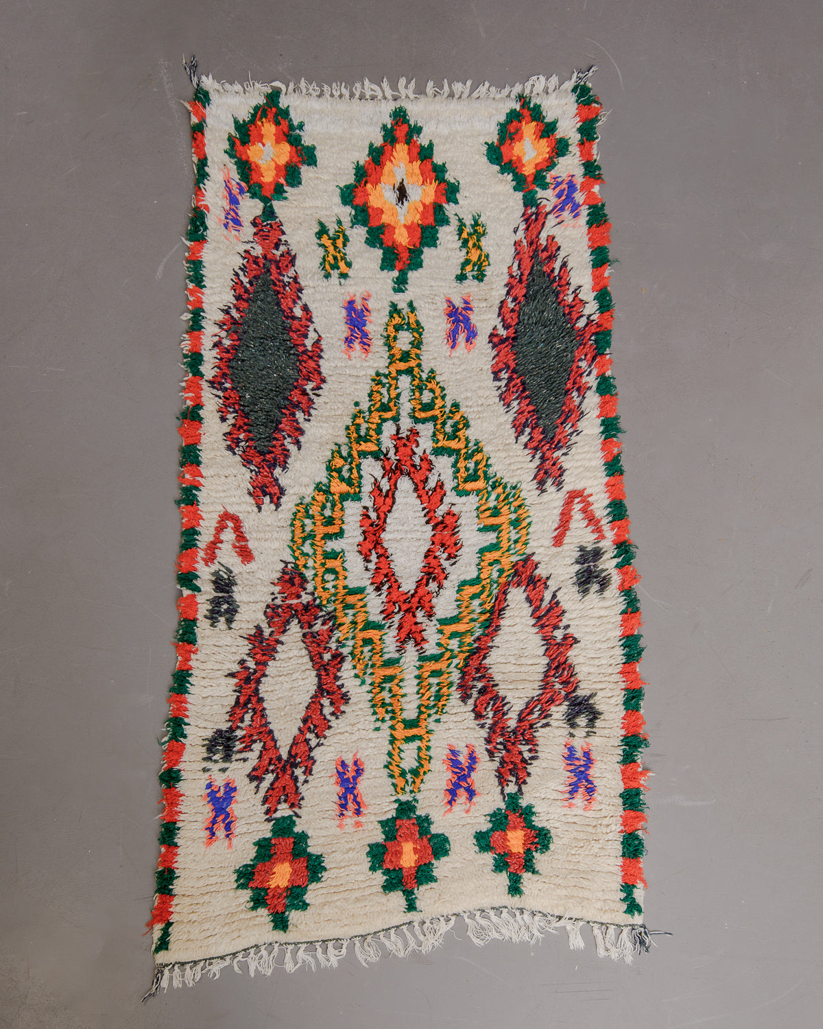 Vintage Berberlin boucherouite runner rug on grey floor in front of velvet curtains.