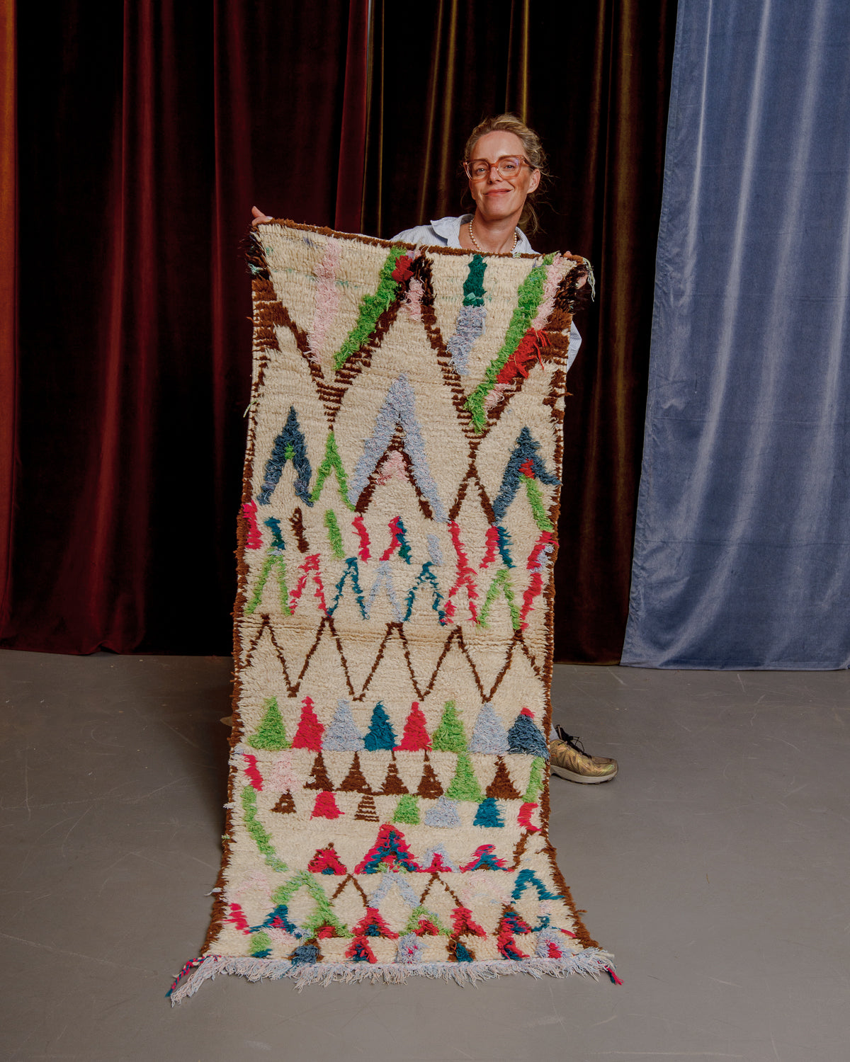 Vintage Berberlin boucherouite runner rug being held up in front of a velvet curtain. 