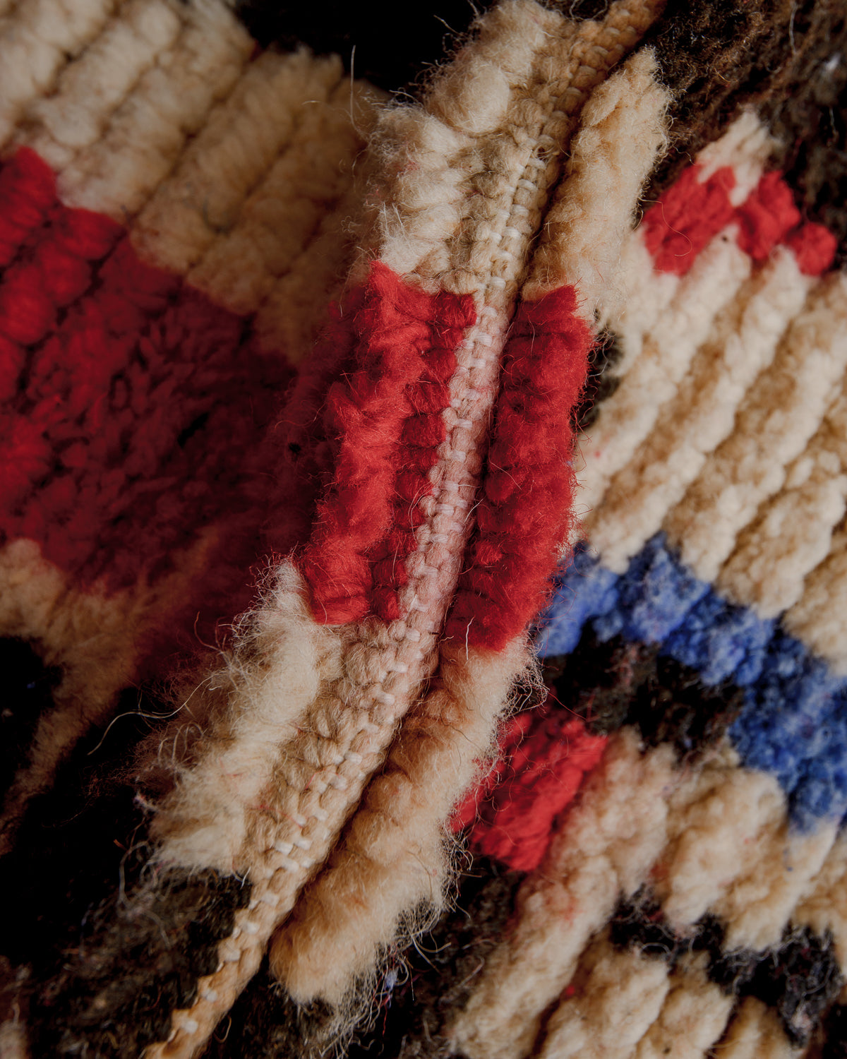 Texture of boujaad rug with beige, red and blue wool.