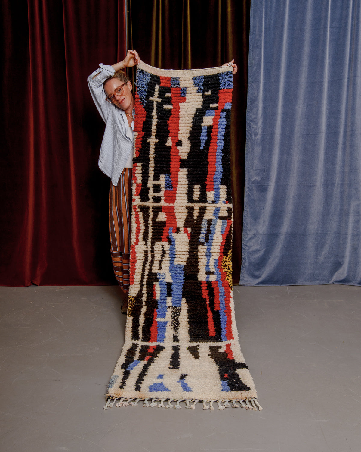Vintage Berberlin boujaad runner rug being held up by a woman in glasses in front of velvet curtains.