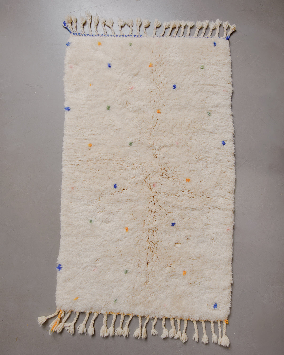 Cream wool rug with coloured dots on grey floor.