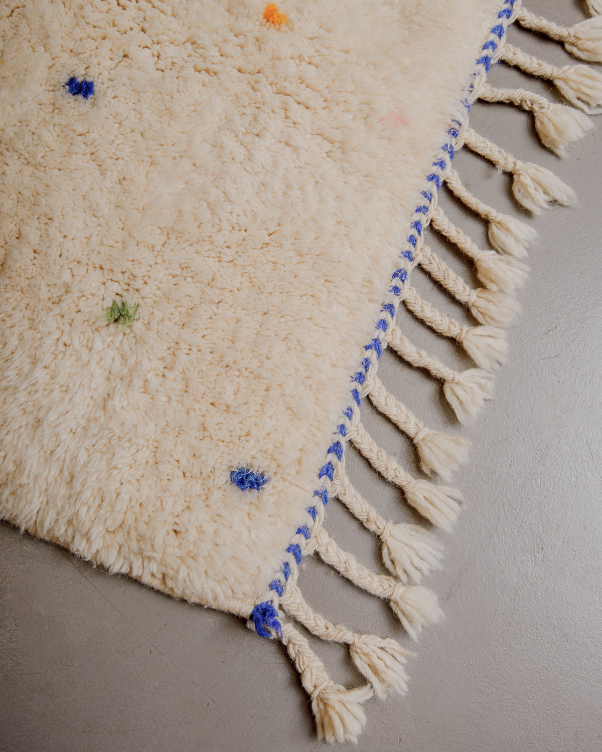 Corner of Berberlin finest rug with fluffy wool, blue woven across the end and natural wool tassels. 