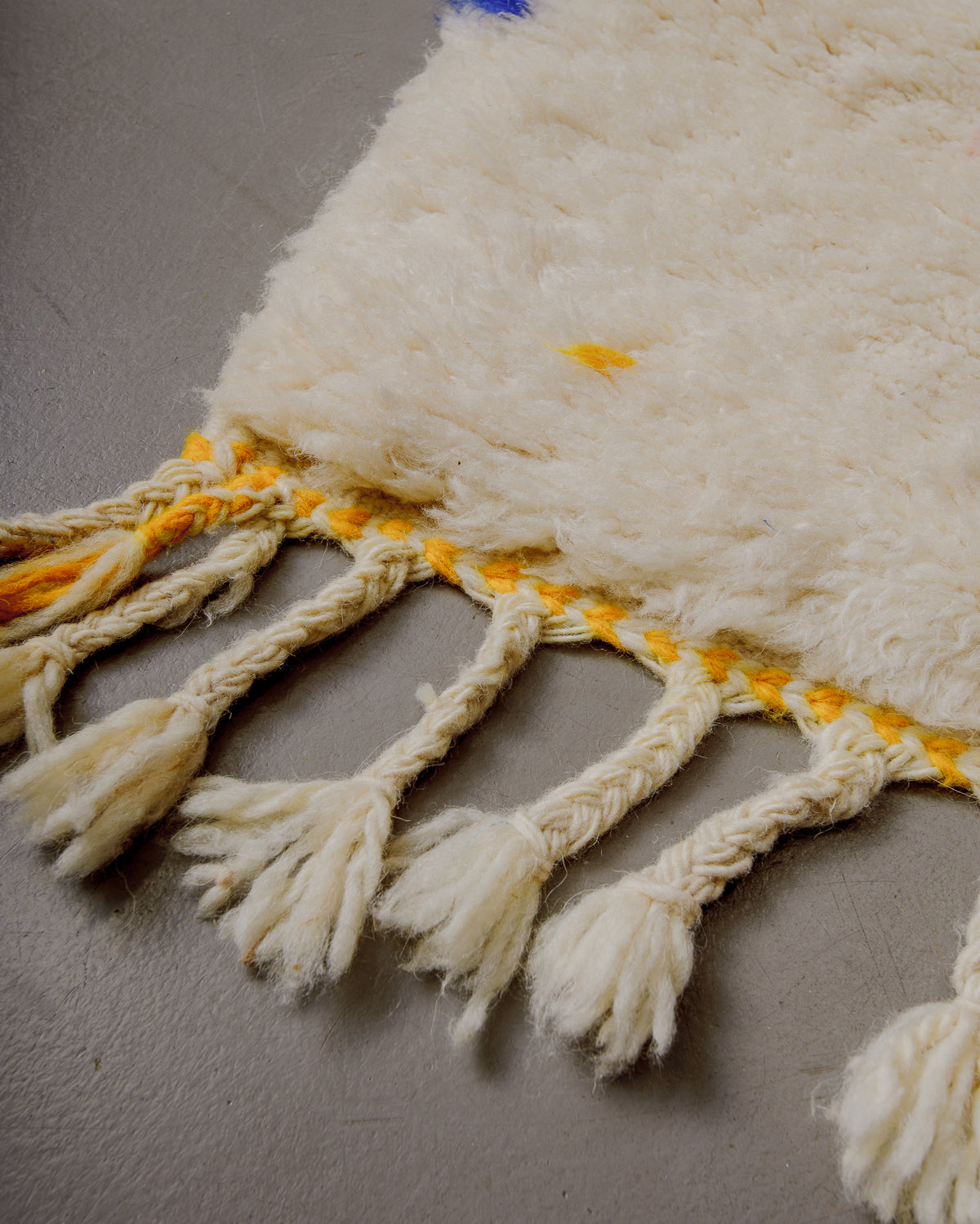 Corner of Berberlin finest rug with fluffy wool, yellow woven across the end and natural wool tassels. 