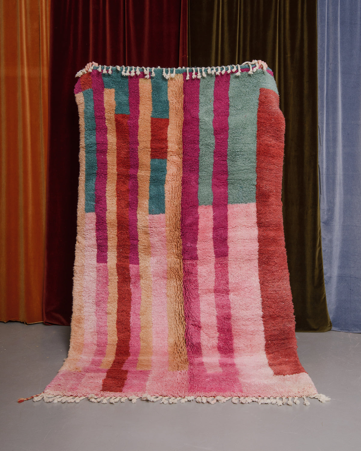 Berberlin Finest beniourain rug held in front of velvet curtains. 