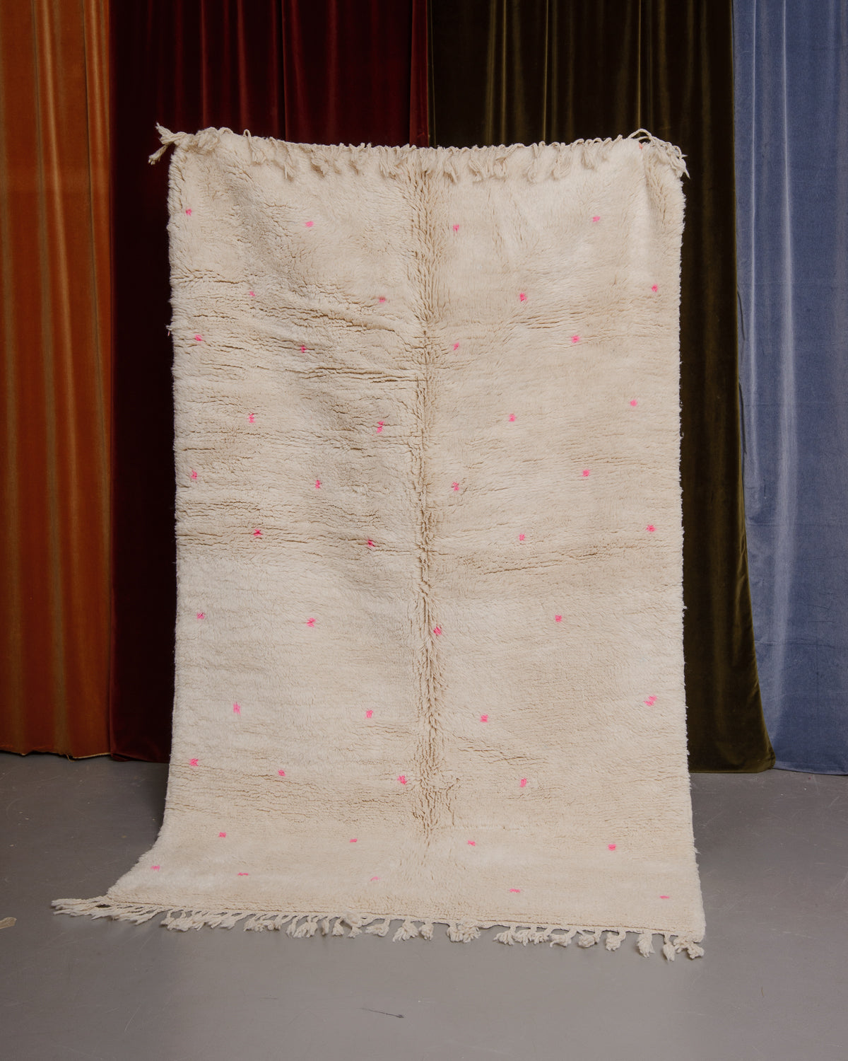 Berberlin Finest beniourain rug held in front of velvet curtains. 