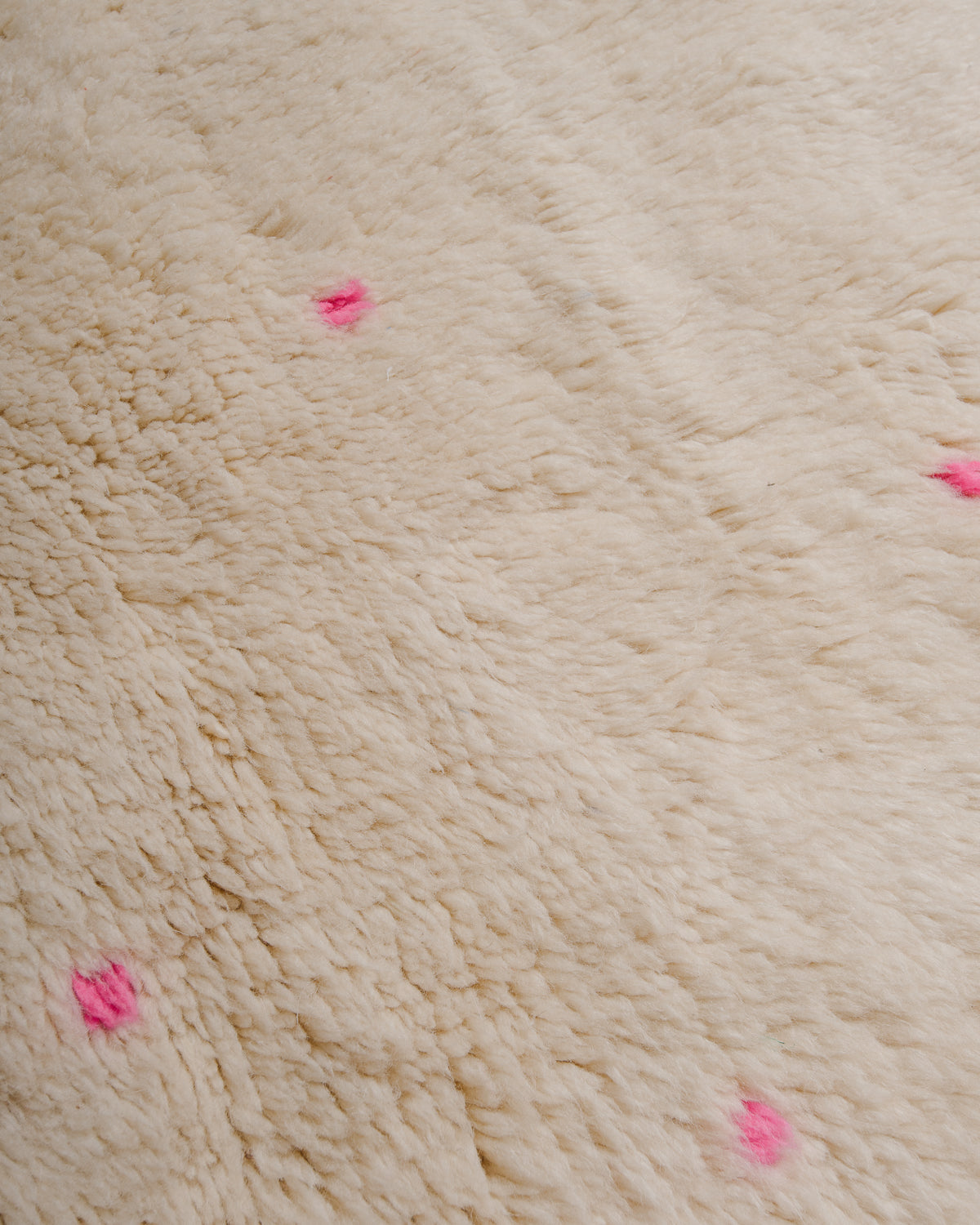 Surface of cream wool rug with small, widely spaced polka dots in neon pink.