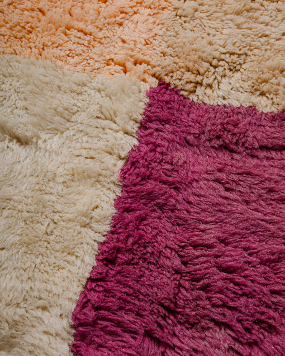 Close up of rug surface with soft apricot, magenta, cream and beige coloured wool.
