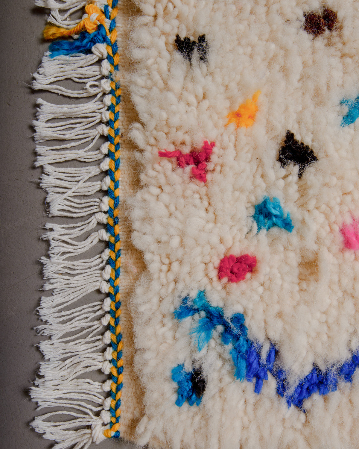 Edge of rug with white cotton tassels and blue and yellow woven along the edge.
