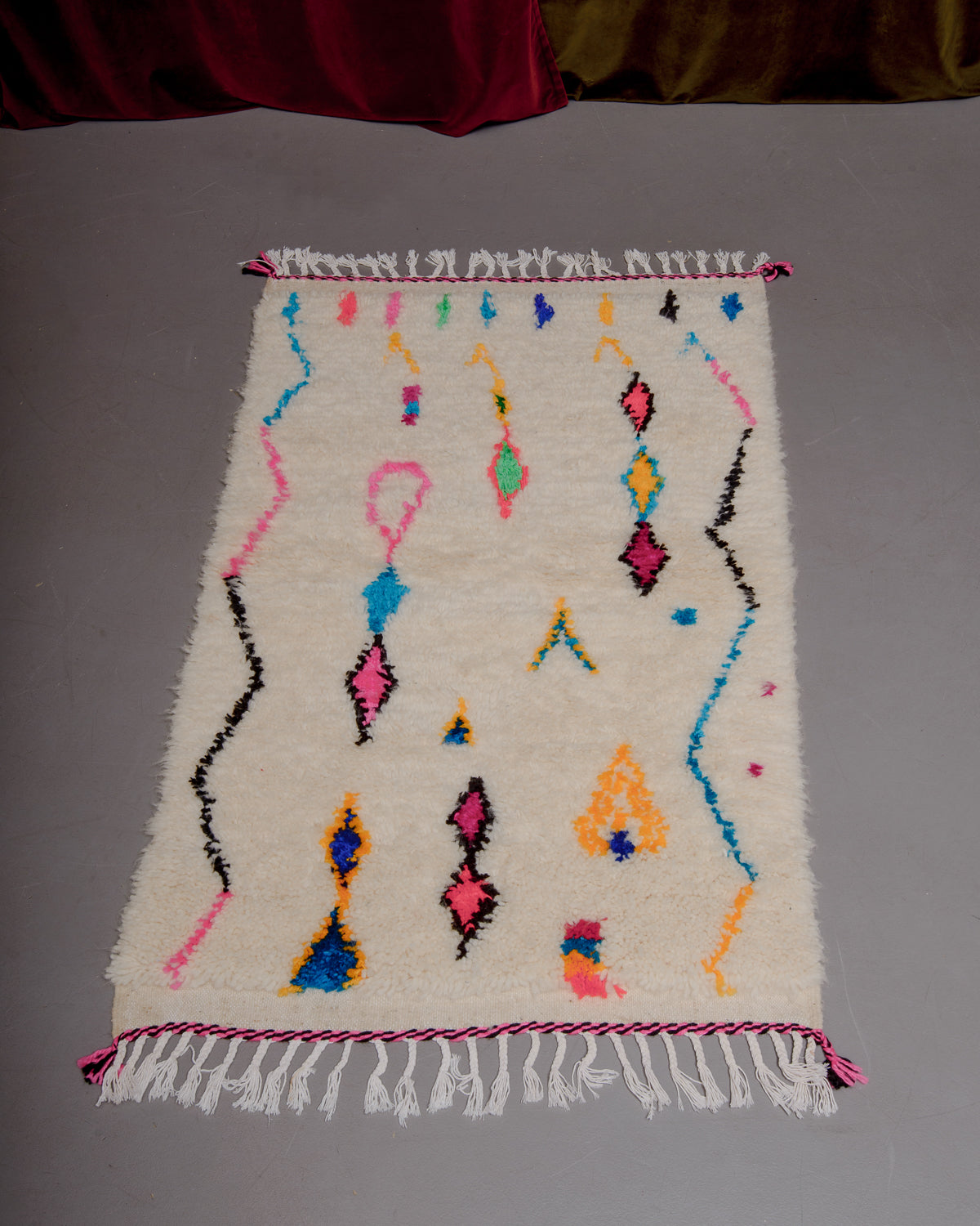 Small Berberlin Azilal rug on grey floor in front of velvet curtains.