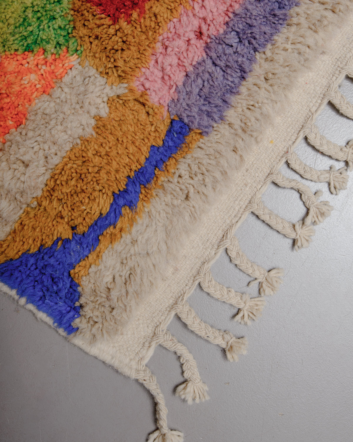 Corner of rug with flat woven edge and natural wool tassels.