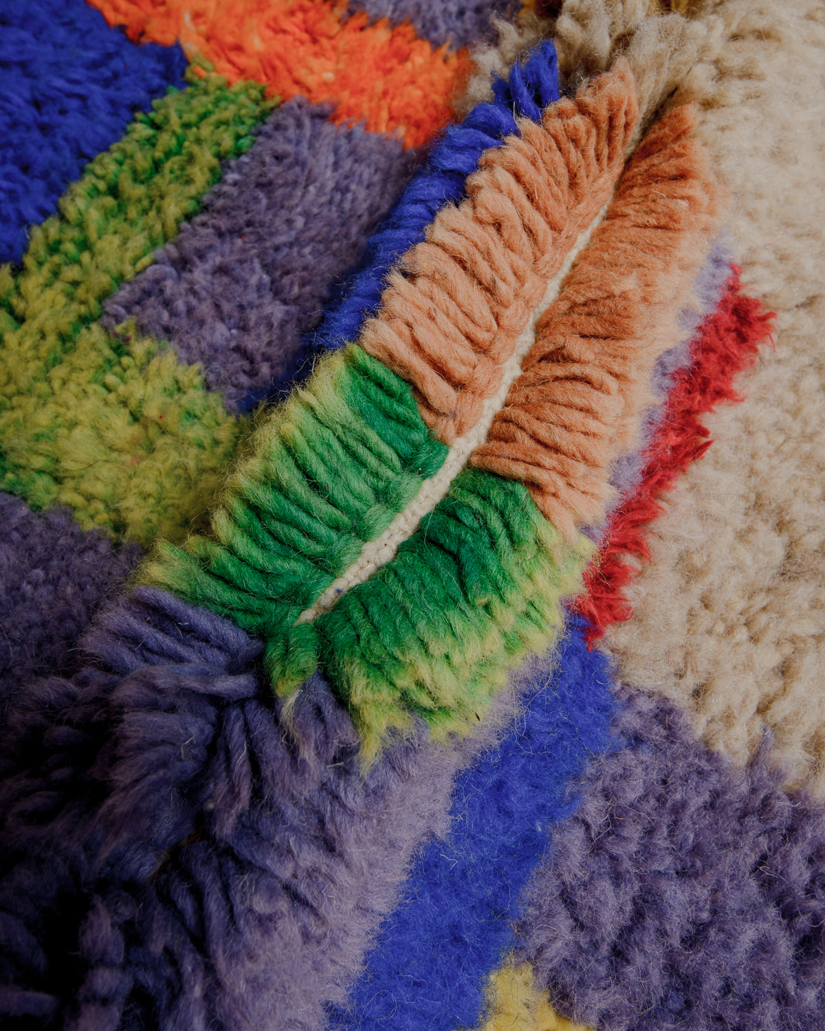 Close up of wool rug showing dense pile made with green, purple and cognac wool.