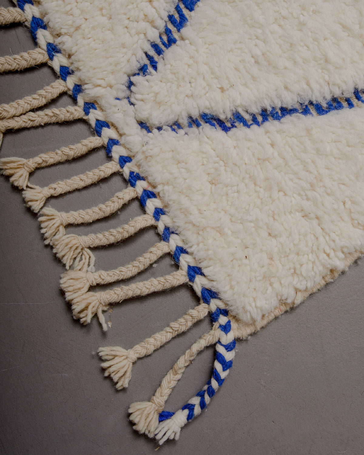 Corner of rug with a blue and white edge and natural wool tassels.