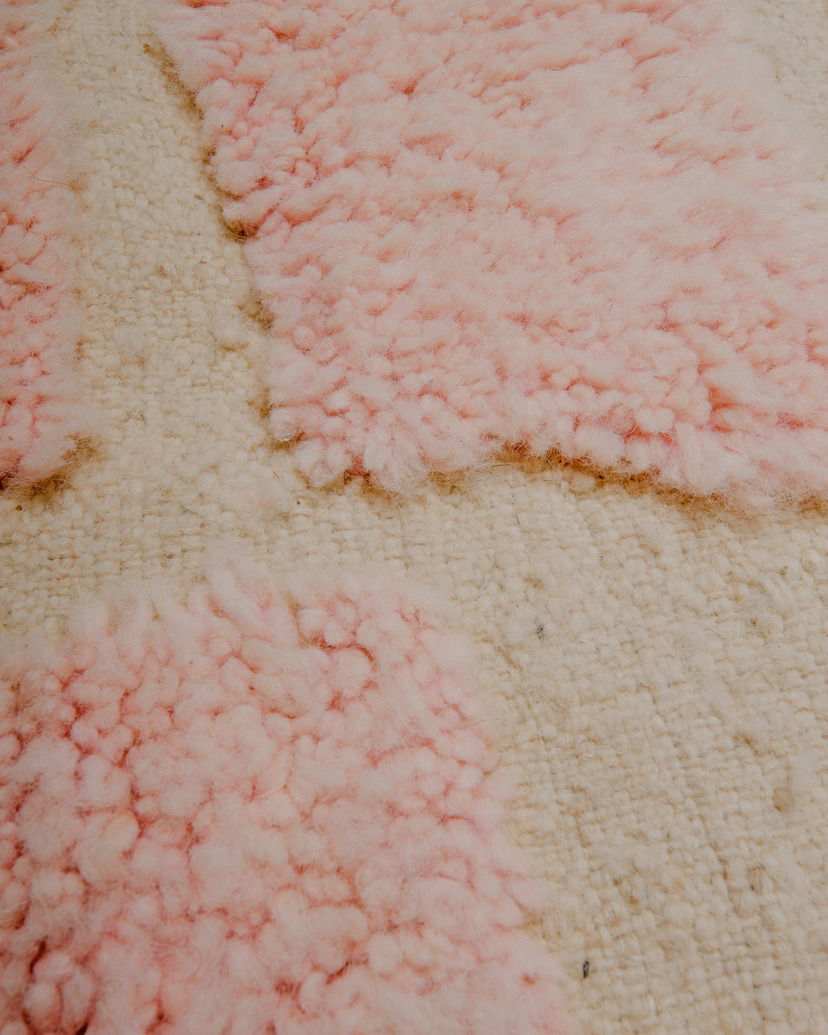 Surface of wool rug with a combination of fluffy pile in pale pink and flat woven areas.