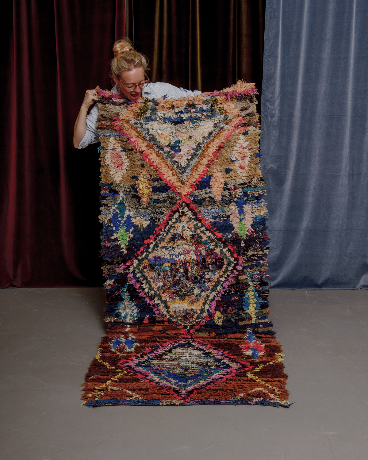 Vintage Berberlin boucherouite runner rug being held up in front of velvet curtains. 