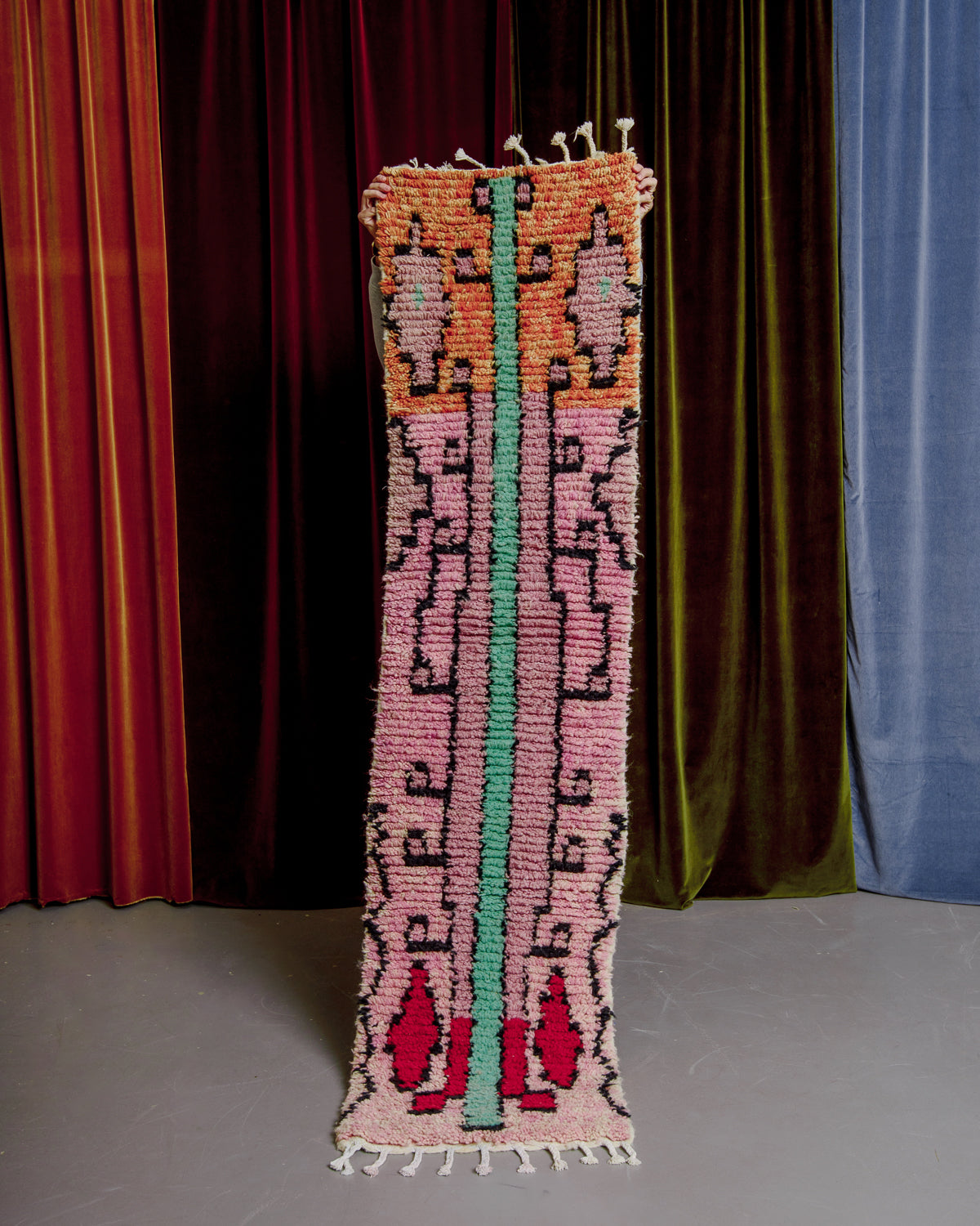 Vintage Berberlin boujaad runner rug being held up in front of velvet curtains.