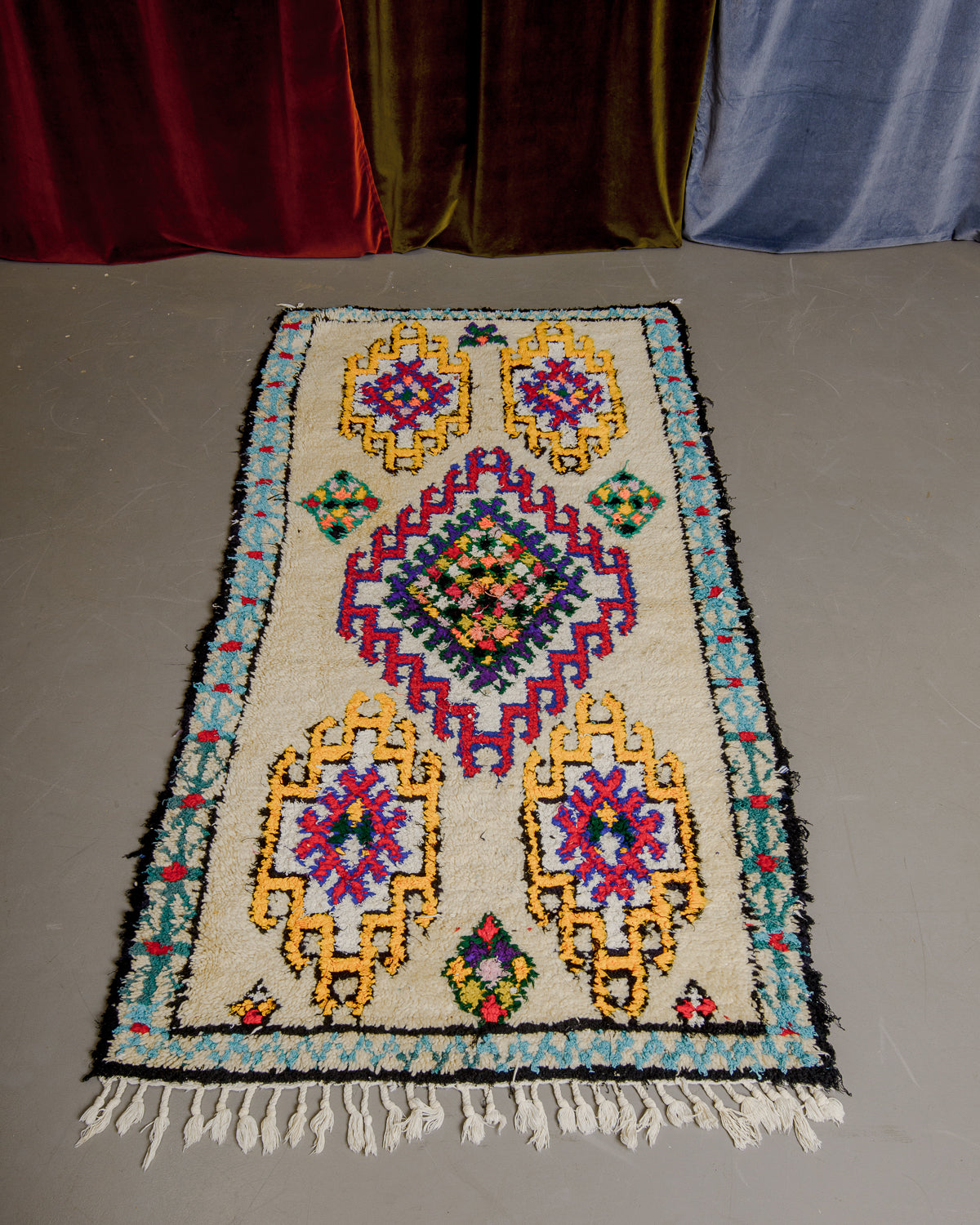 Vintage Berberlin boucherouite runner rug on grey floor in front of velvet curtains.