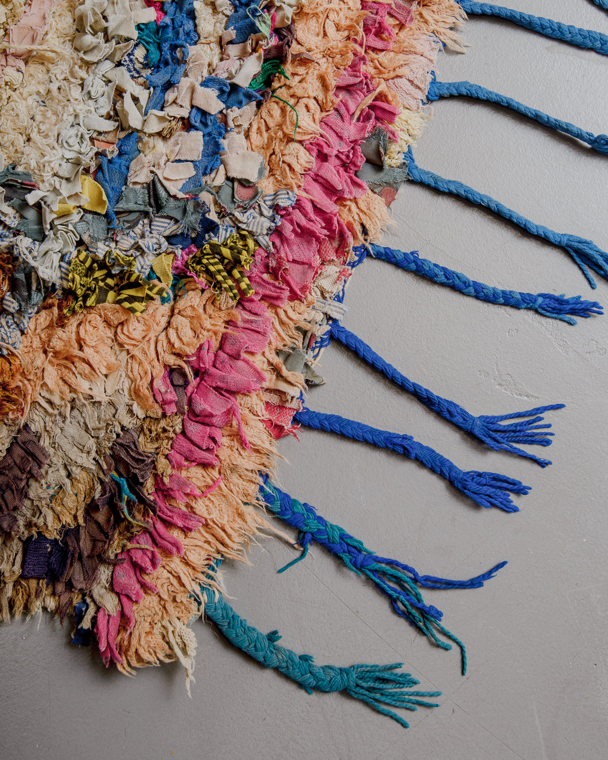 Corner of boucherouite rug with cotton tassels in different shades of blue.
