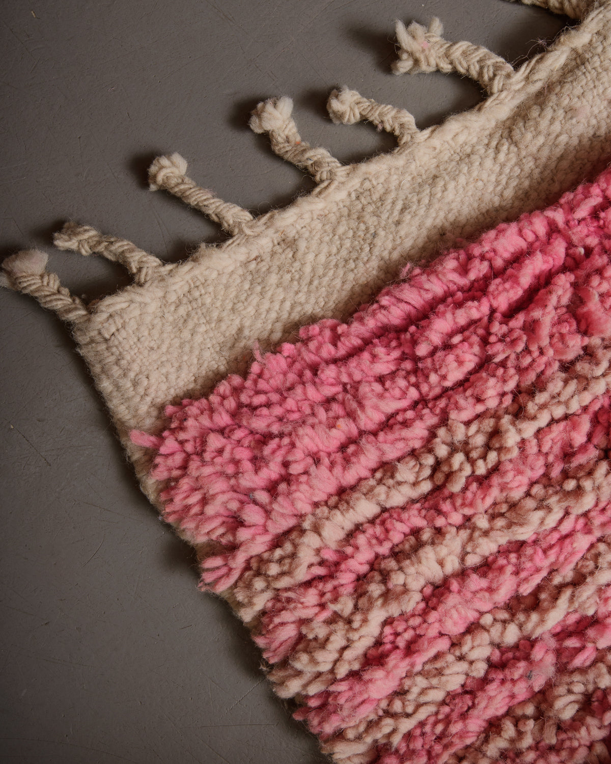 Corner of vintage wool rug with textured pile and flat woven edge with natural wool tassels. 