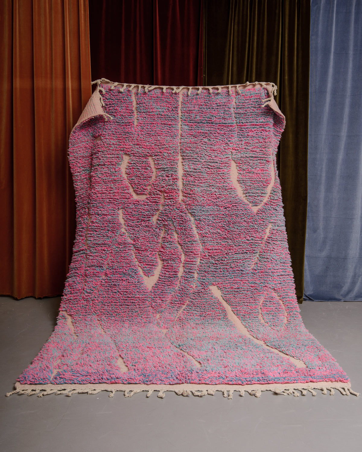 Berberlin Boujaad rug in pink and blue speckled wool with organic woven lines being held in front of velvet curtains.