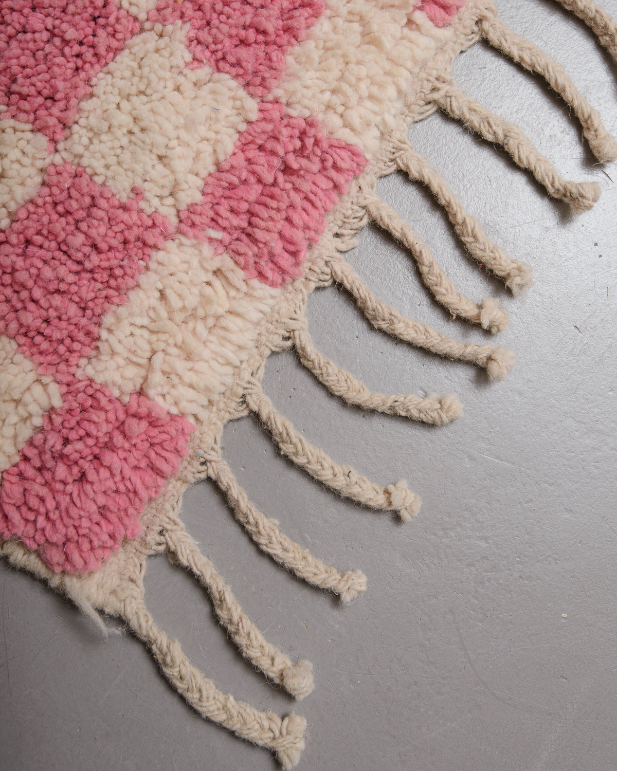 Corner of vintage wool rug with textured pile and flat woven edge with natural wool tassels. 