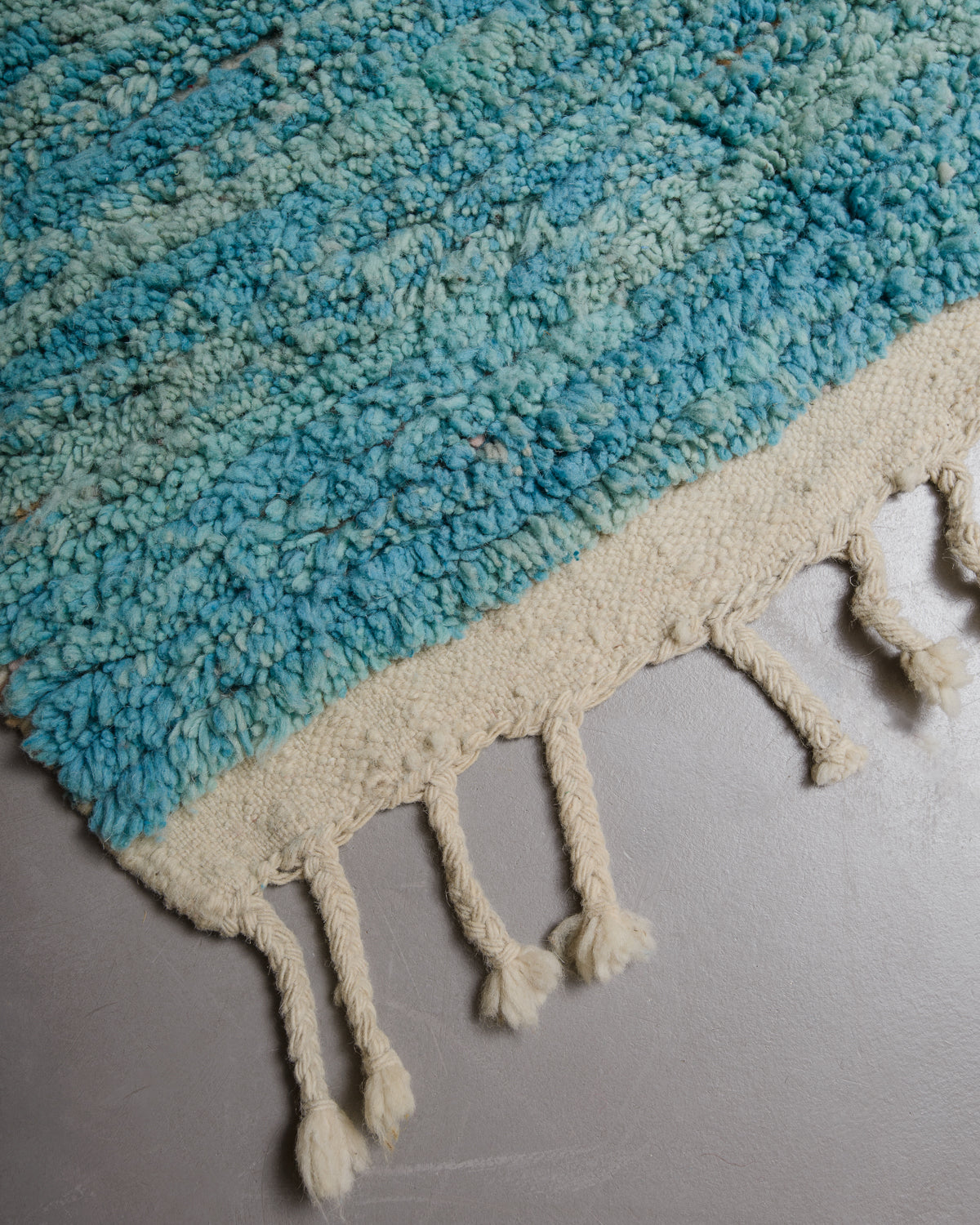 Corner of vintage wool rug with textured pile and flat woven edge with natural wool tassels. 