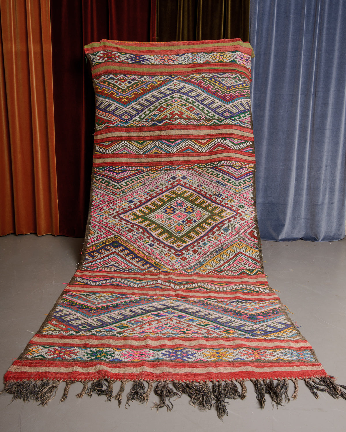 Colourful Vintage Kelim being held in front of velvet curtains. 